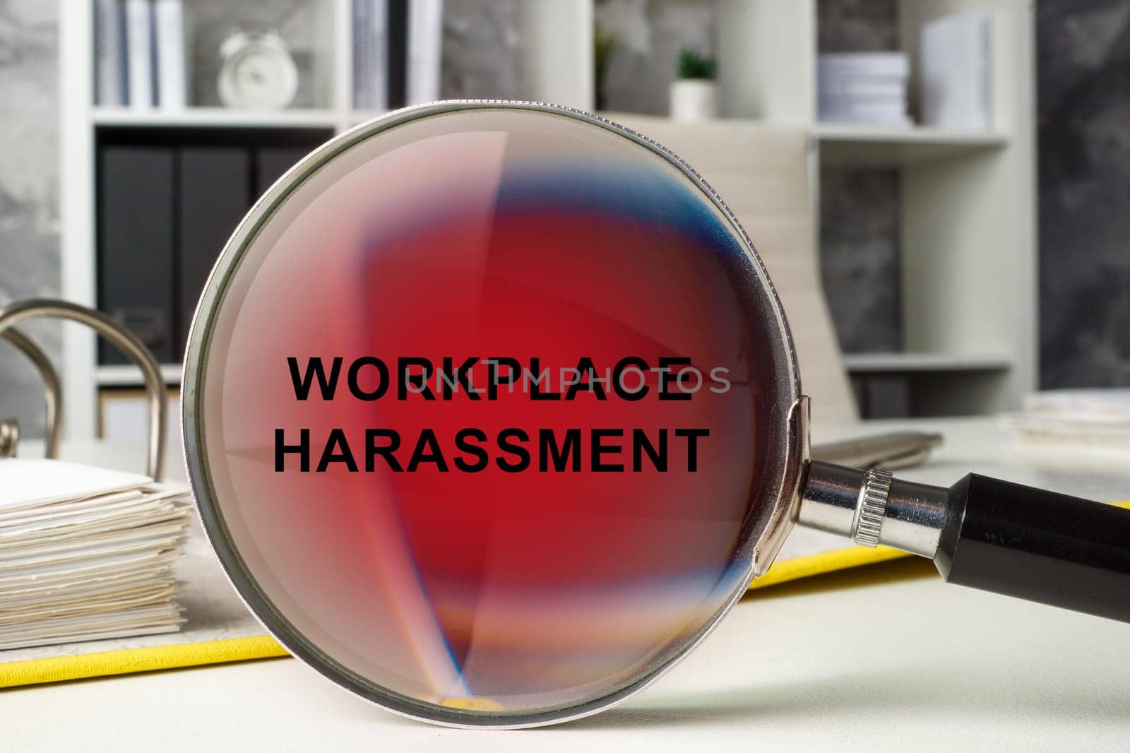 Office workspace and magnifying glass with words workplace harassment. by designer491