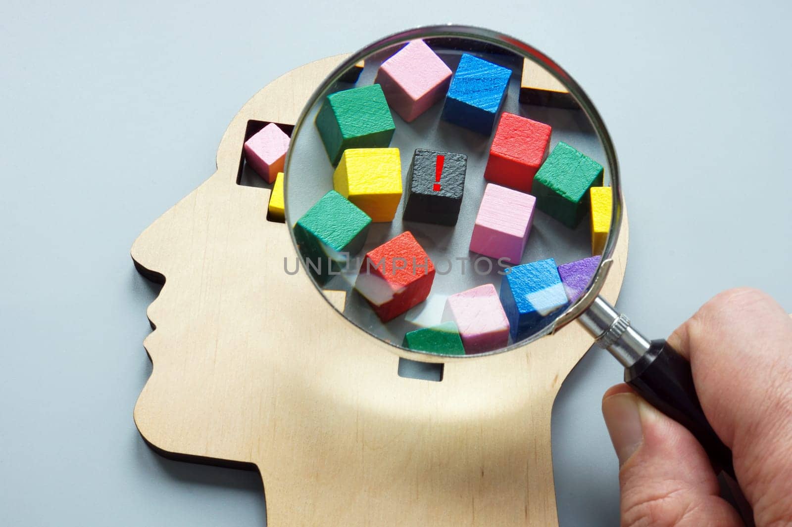 Psychoanalysis and negative emotions. A hand with magnifying glass examines wooden head.