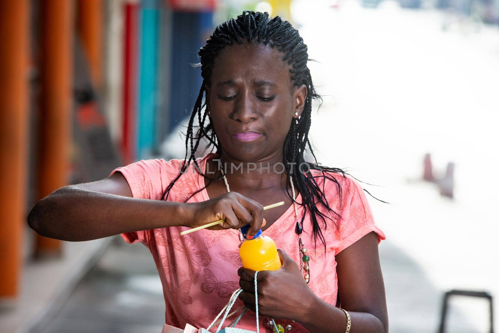young girl standing outdoors opening a bottle of fruit juice.