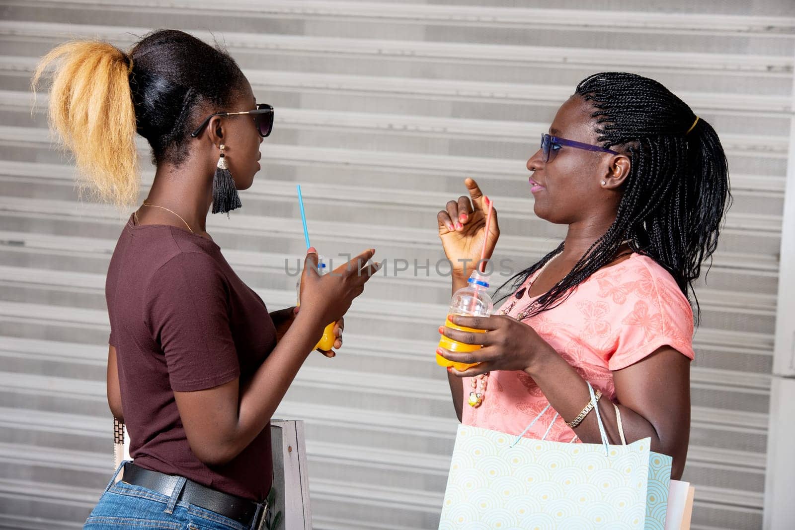 young girls standing in sunglasses with bottles of fruit juice chatting after shopping
