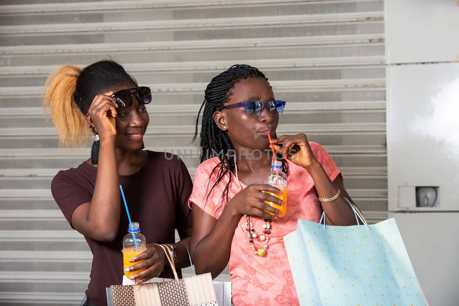 Young girls standing in glasses watching something with bottles of juice in hand after shopping.