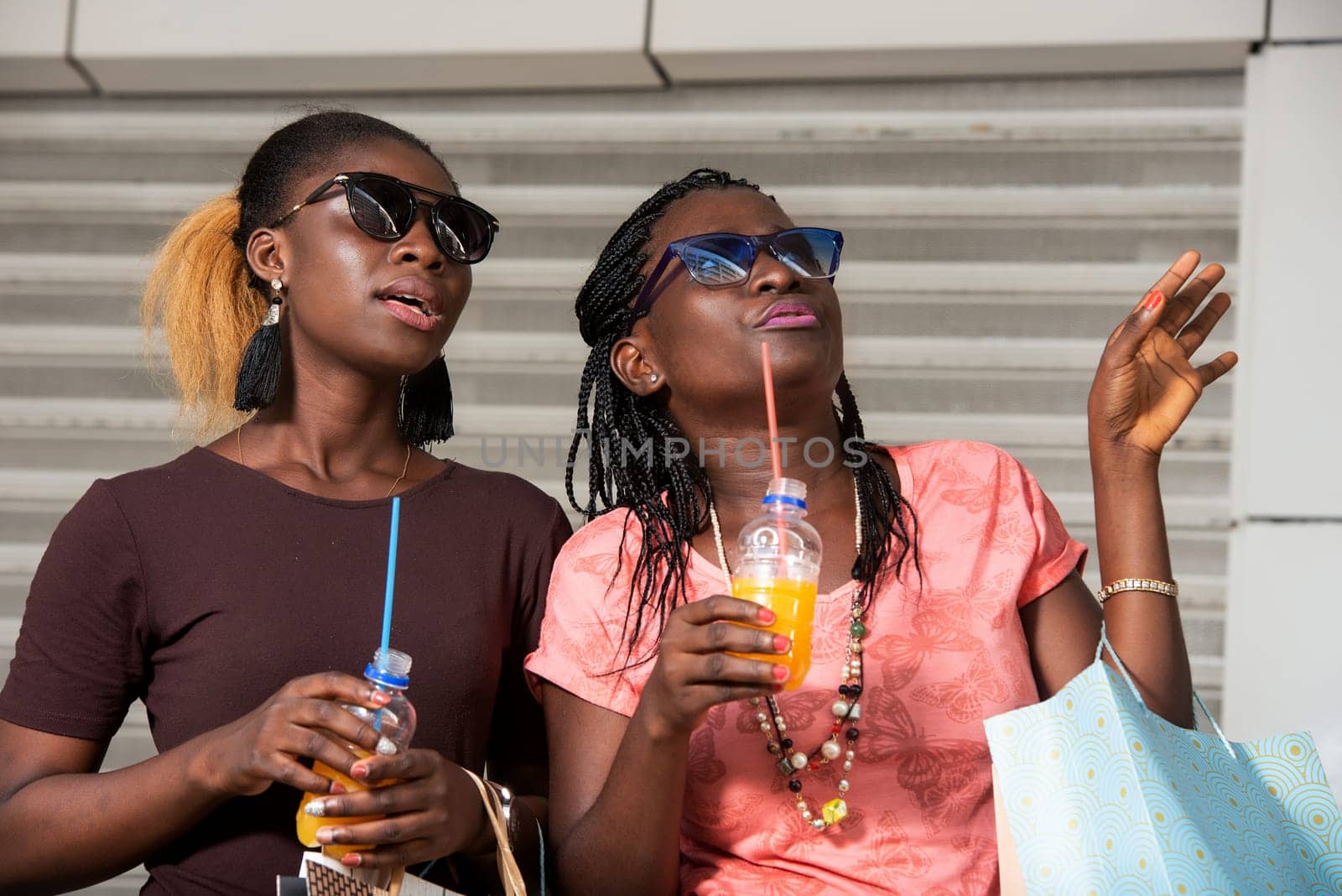 Young girls standing in glasses looking up there with bottles of juice in hand after shopping.