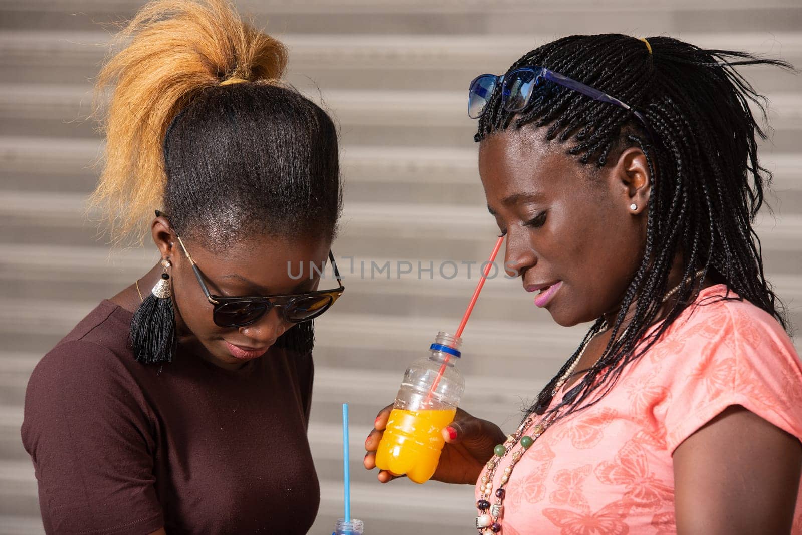Young girls standing in sunglasses looking in shopping bags with bottles of juice in hand.