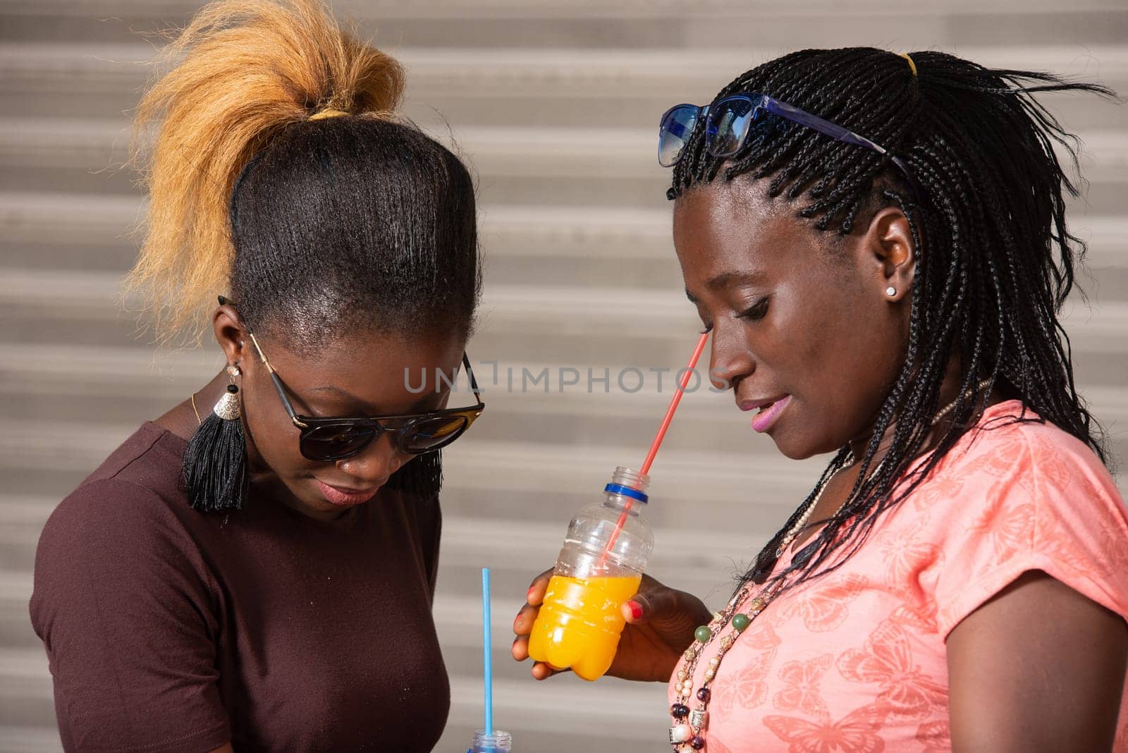 Young girls standing in sunglasses looking in shopping bags with bottles of juice in hand.