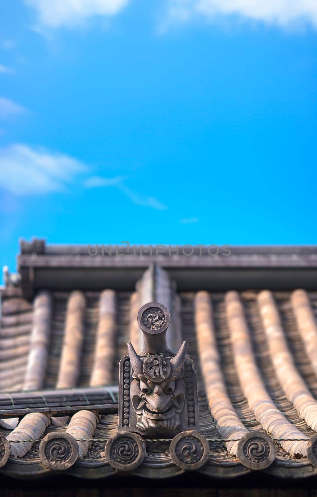 Traditional Japanese tiled roof of Buddhist temple decorated with the furious face of an onigawara gargoyle with horns and fangs and with tiles adorned with a tomoe pattern made up of magatama shapes.