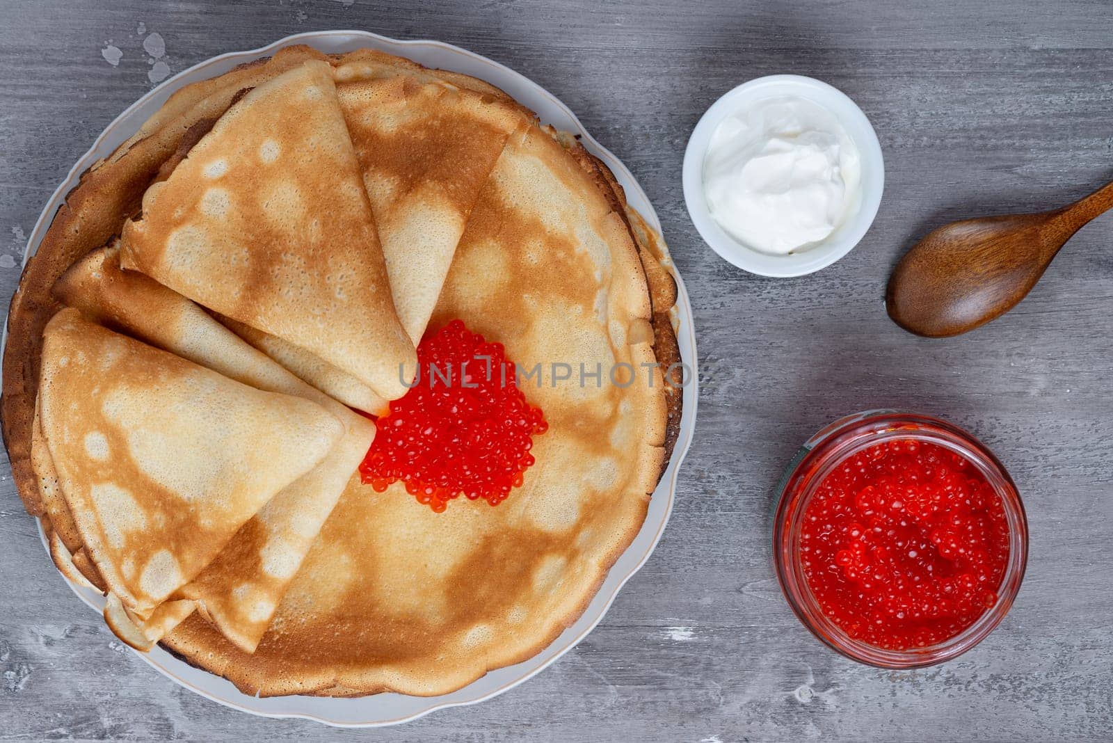 Stack of russian thin pancakes blini with red caviar and fresh sour cream.