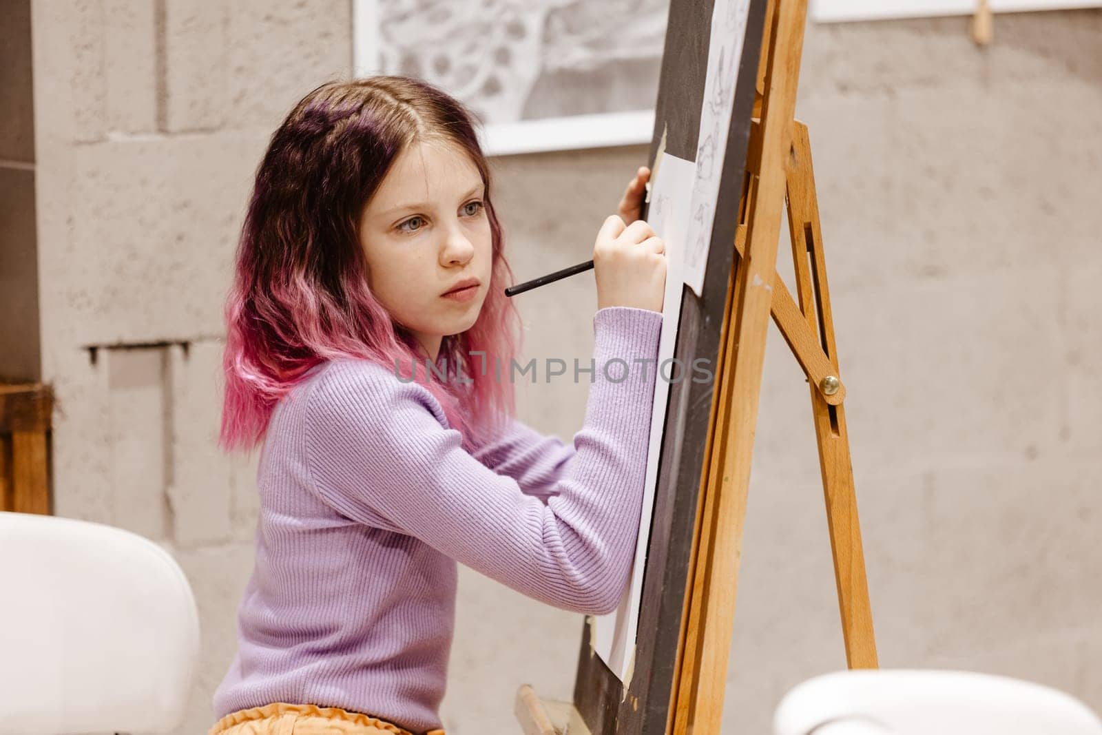 Girl 11 years old craftswoman are painting on canvas in studio standing in front of easel. Portrait of a girl painting during an art class. by sarymsakov