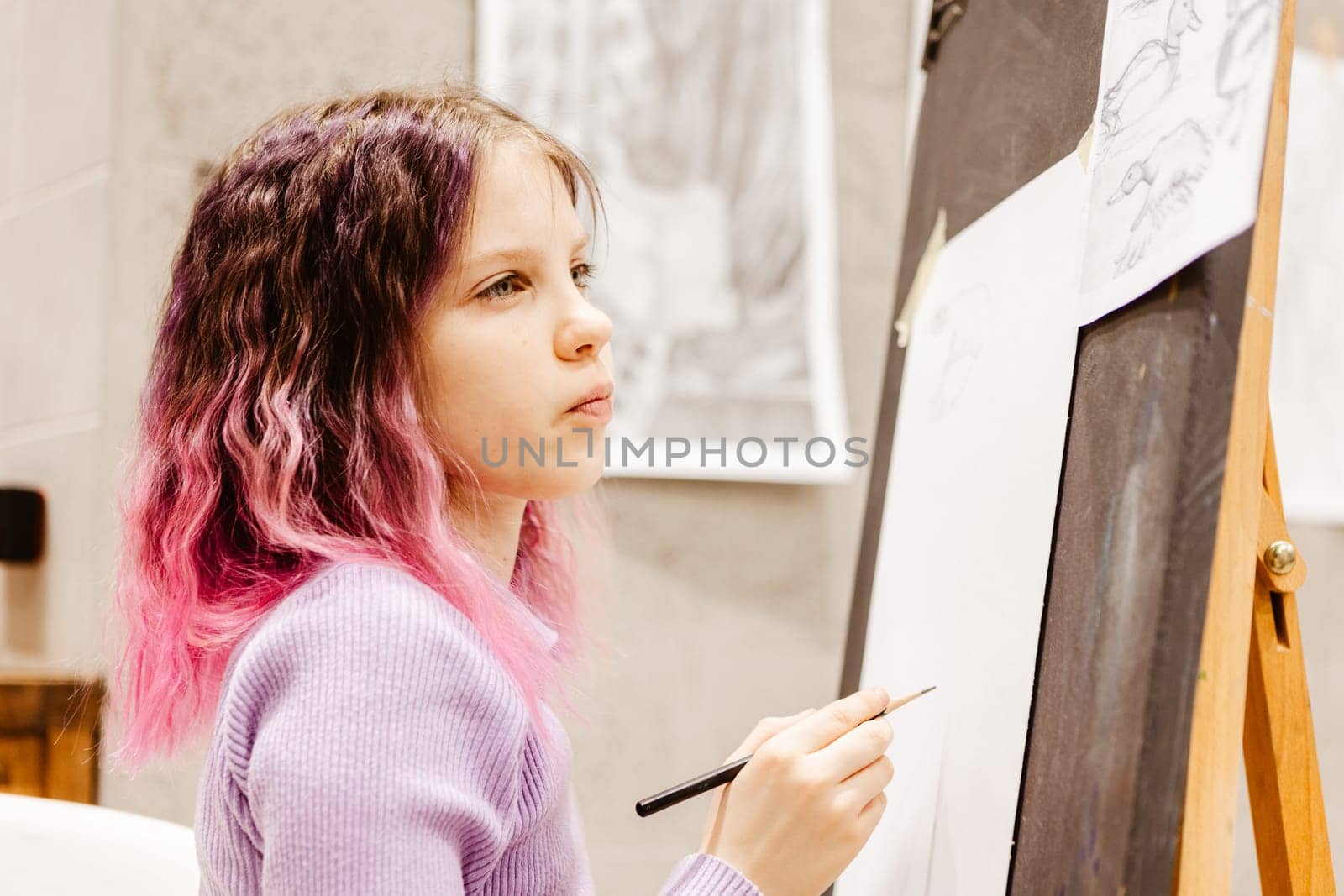 Girl 11 years old craftswoman are painting on canvas in studio standing in front of easel. Portrait of a girl painting during an art class