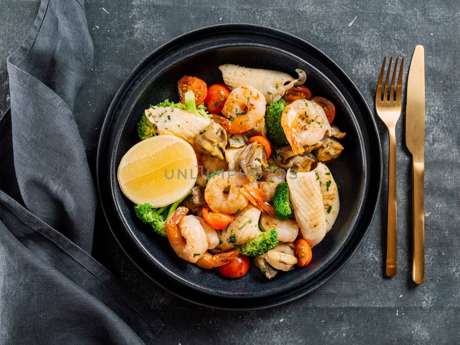 Mixed Seafood Contain Shrimps, Mussels, Calamari Squids and Fish with Broccoli, Cherry Tomato, Lemon on Black dish in restaurant-style platting. Seafood salad on dark background. Top view