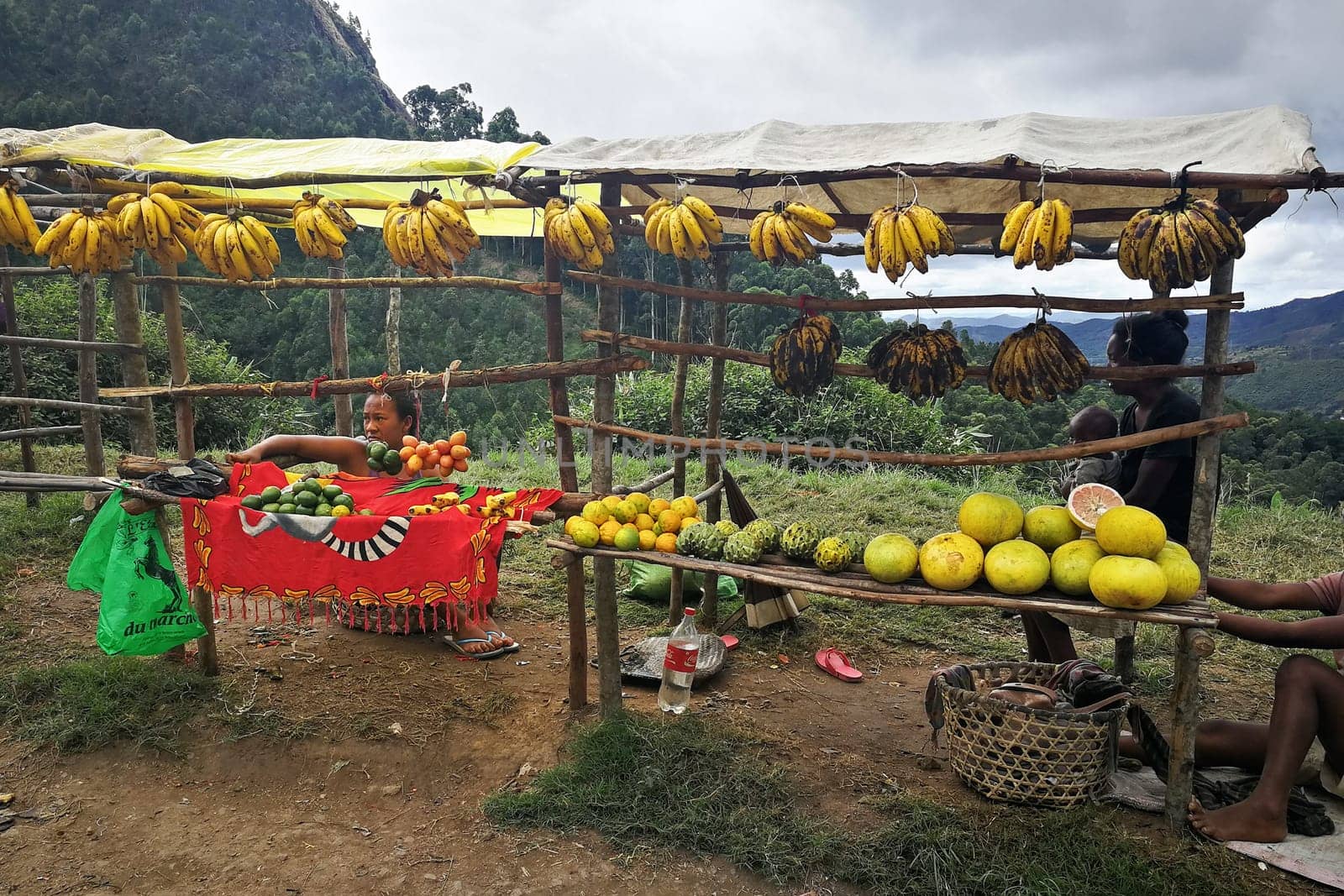 Mandraka, Madagascar - April 24, 2019: Unknown Malagasy locals selling bananas, pomelo and other citrus fruits by the highway. Food is usually sold at roadside, as only few shops exists in this area by Ivanko