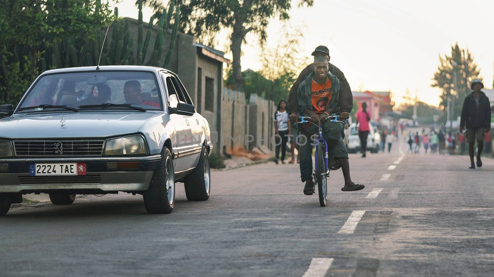 Ranohira, Madagascar - April 29, 2019: Two unknown Malagasy locals riding on one bicycle, car next to them, but most people are just walking as they're too poor in this region to afford any transport by Ivanko