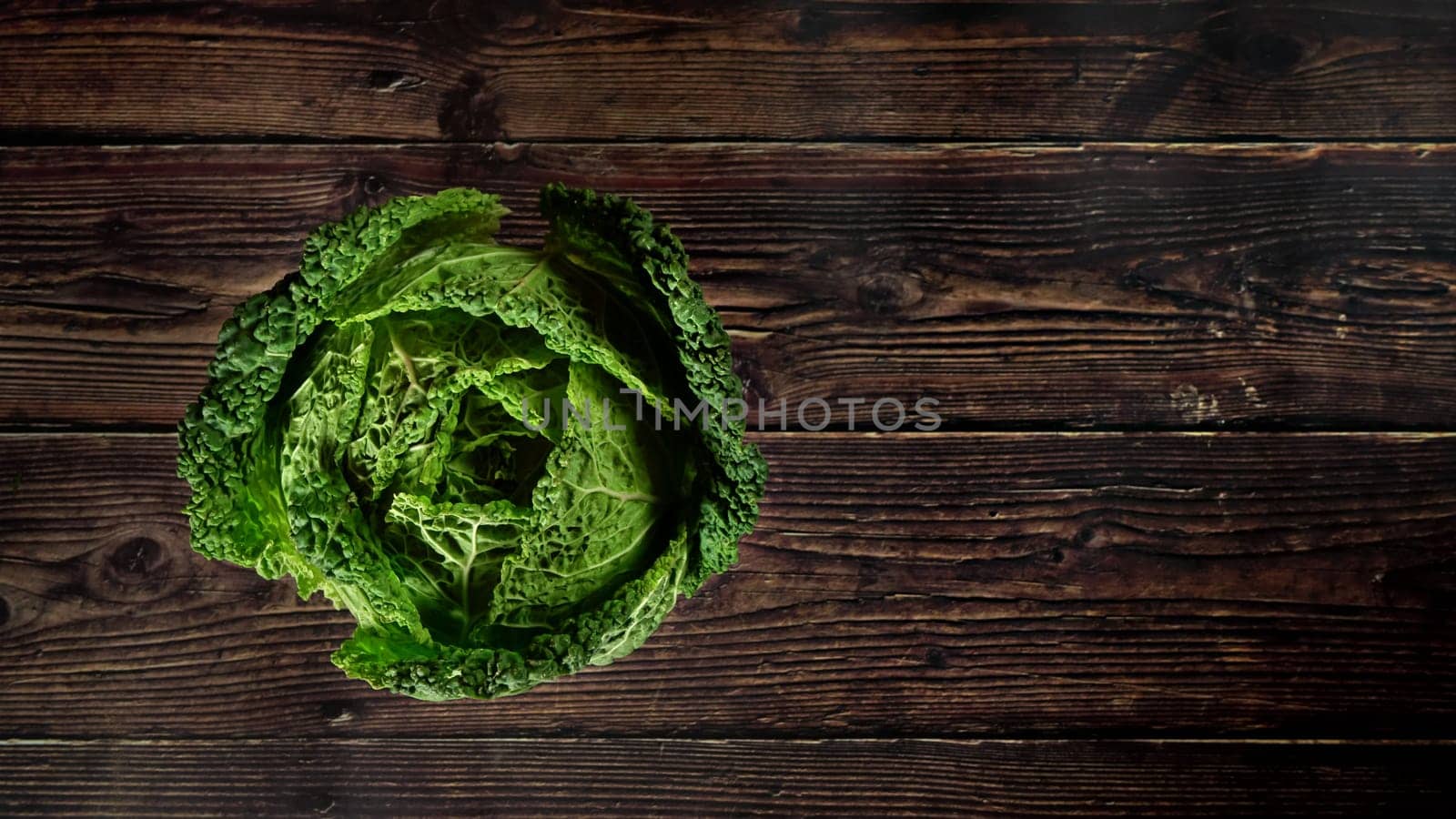 Top down view, single raw savoy kale cabbage on dark wooden board, wide banner space for text right side by Ivanko
