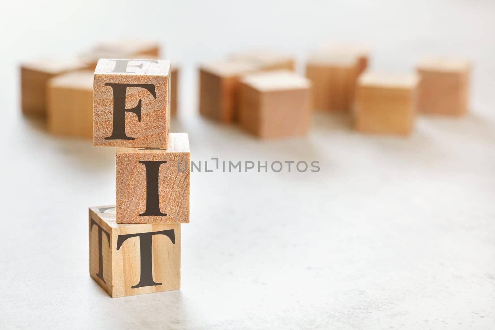 Three wooden cubes with word FIT, on white table, more in background, space for text in right down corner