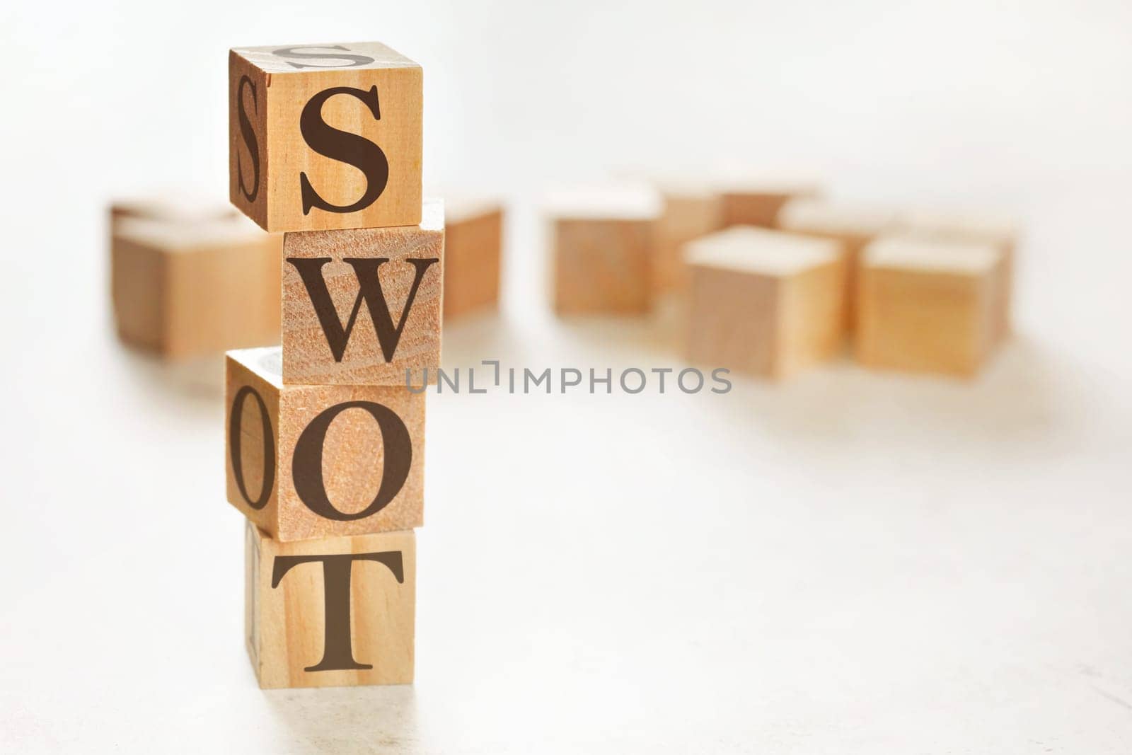 Four wooden cubes arranged in stack with text SWOT (meaning Strengths, Weaknesses, Opportunities and Threats) on them, space for text / image at down right corner