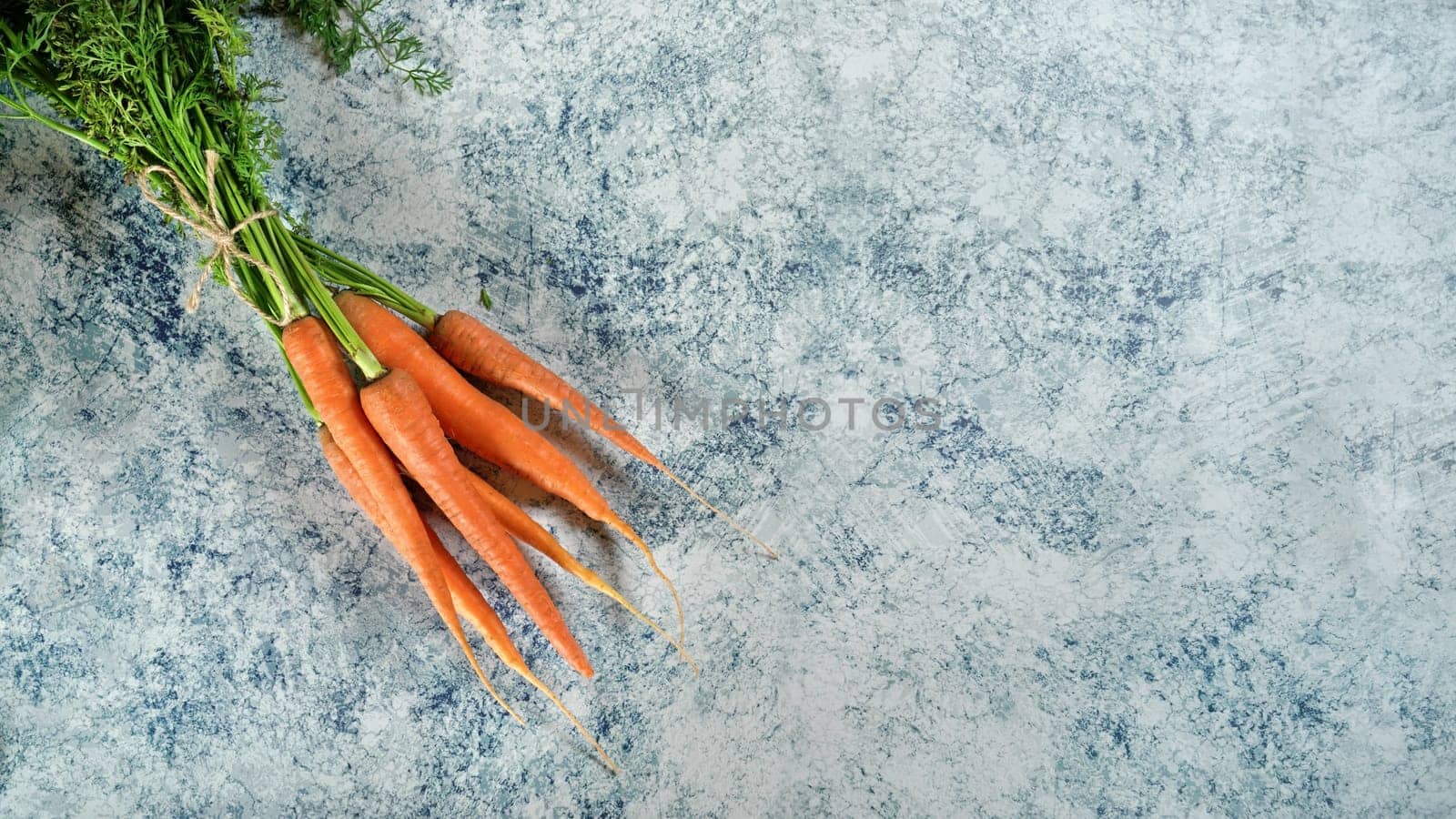 Bunch of carrots with green leaves on blue marble like board, view from above