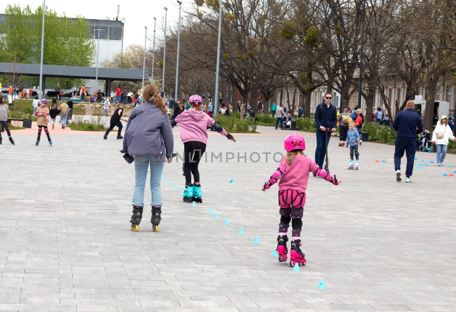 Ukraine. Kyiv. 23.04.2023. children, teenagers playing roller skates with friends outdoors. lot of children, kids go rollerblading, learn roller-skating with an adult instructor, having break in shade