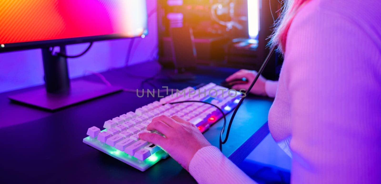 Close up hand of gamer playing cyber video game online with personal computer keyboard at home, woman actively pushing gaming keyboard buttons in the neon room