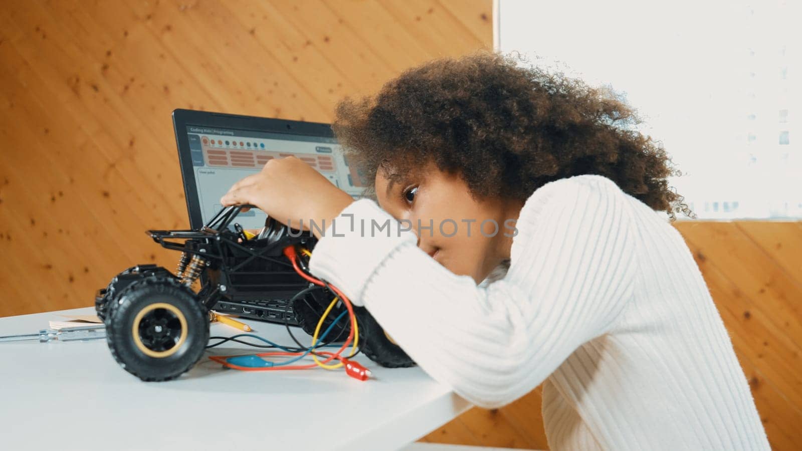 Smart african girl build robotic car while using wires while using laptop setting or writing prompt code. Skilled female student working on computer in STEM technology online classroom. Erudition.