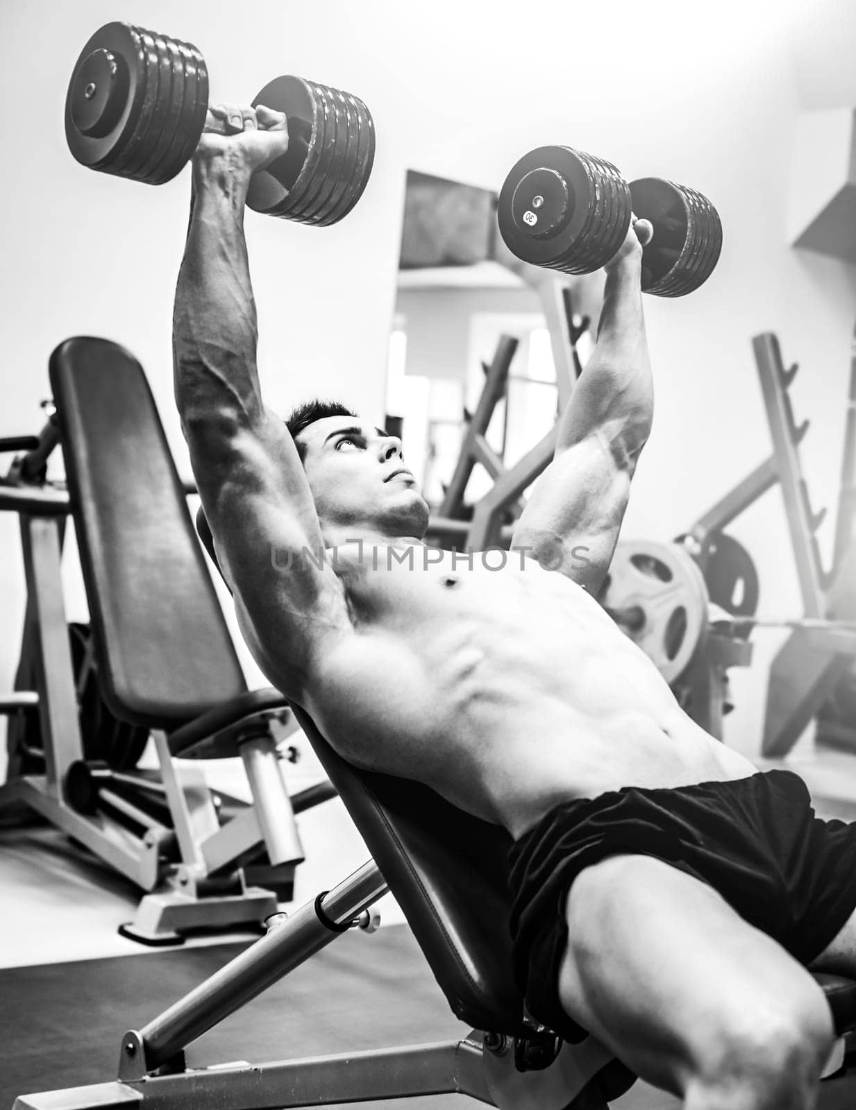 Strong muscular bodybuilder man pressing dumbbells in a gym by GekaSkr