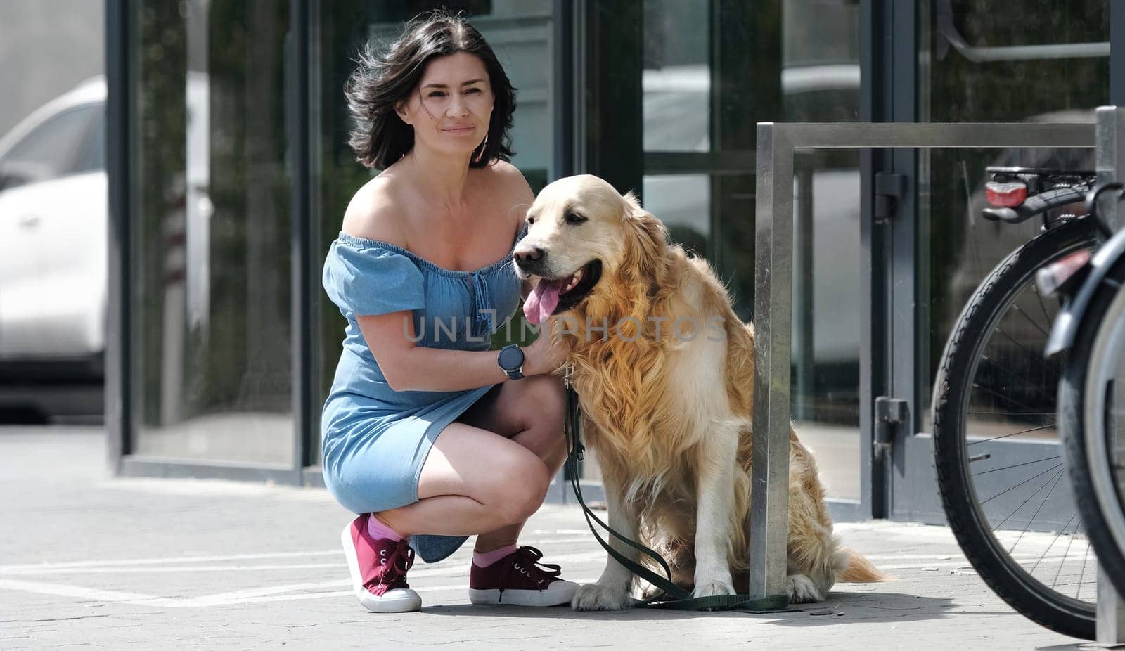 Golden retriever dog on leash and pretty girl sitting at street near supermarket. Purebred pet doggy and young woman together outdoors in city