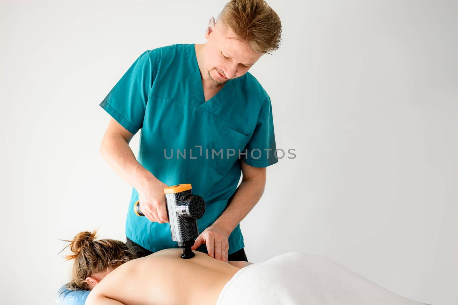 Masseur man doing back massage to girl client using professional massager machine. Body care treatment therapy procedure for wellness and relaxation in spa salon clinic with special tool.