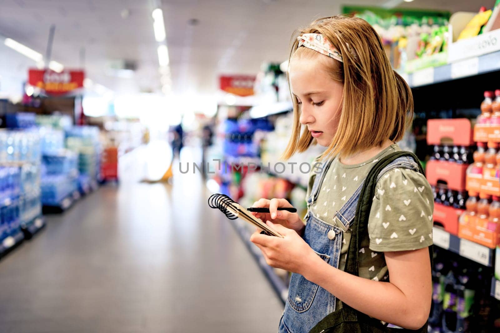 Pretty girl child buying with shopping list in supermarket and checking products. Beautiful female preteen kid in grocery store