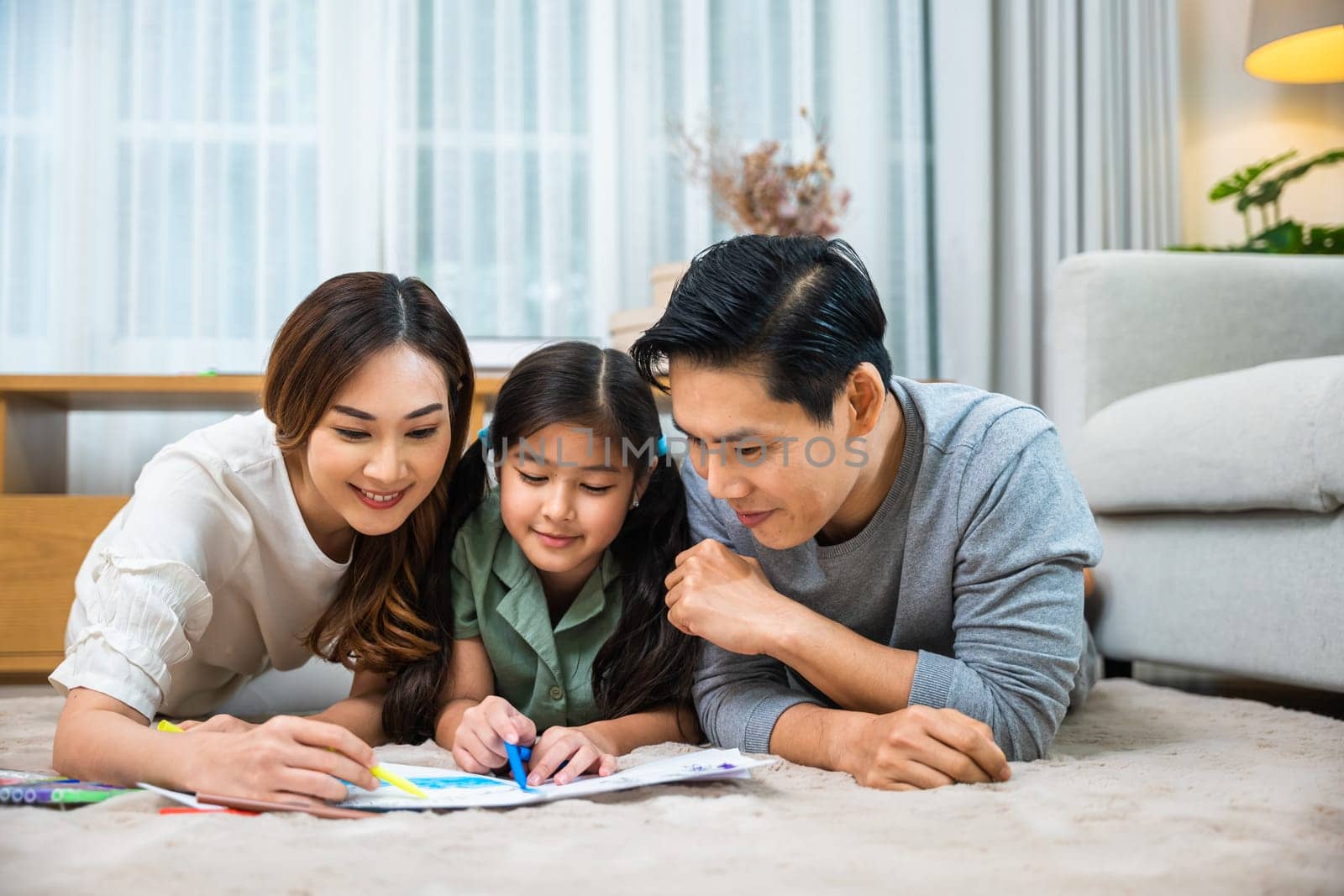 Smiling Father, Mother and daughter drawing together on paper at home by Sorapop