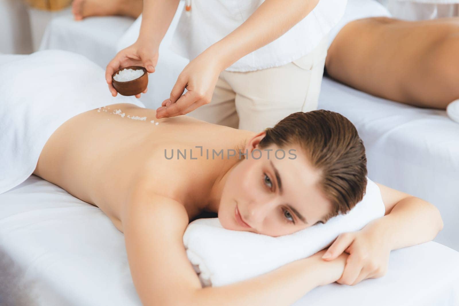 Woman customer having exfoliation treatment in luxury spa salon with warmth candle light ambient. Salt scrub beauty treatment in health spa body scrub. Quiescent