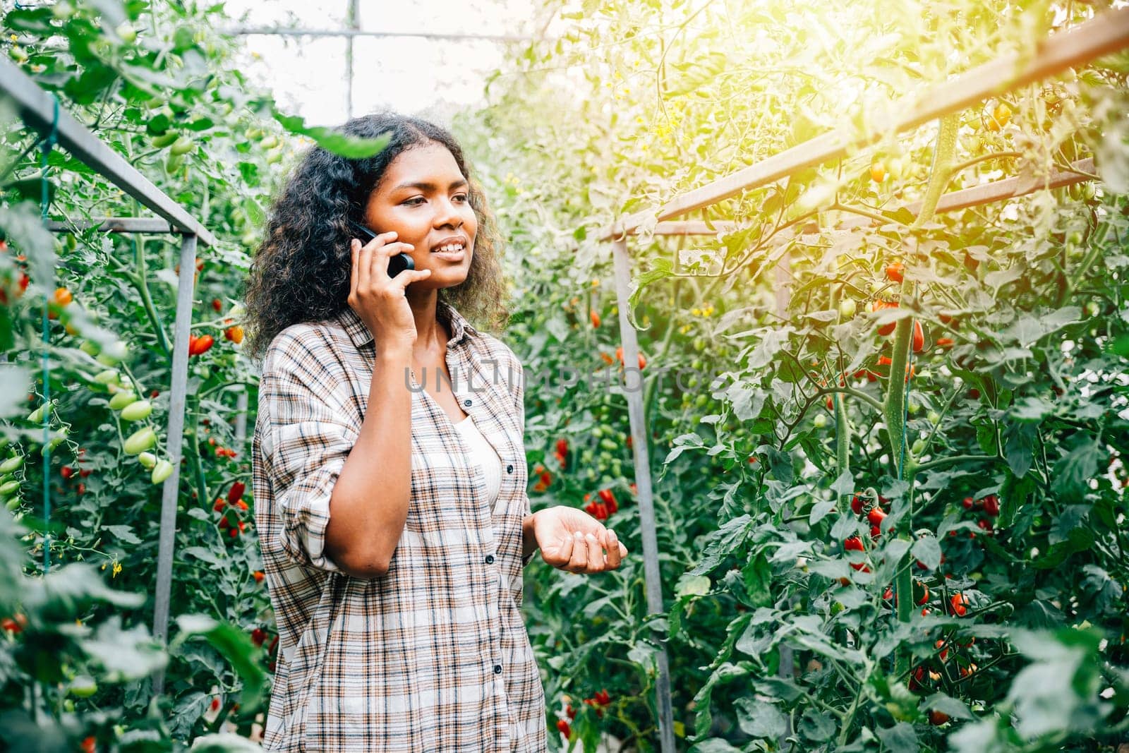 Woman farmer in greenhouse talks on phone by Sorapop