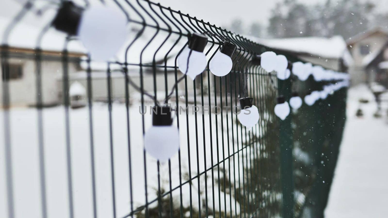 A white garland of bulbs on a fence in winter. by DovidPro