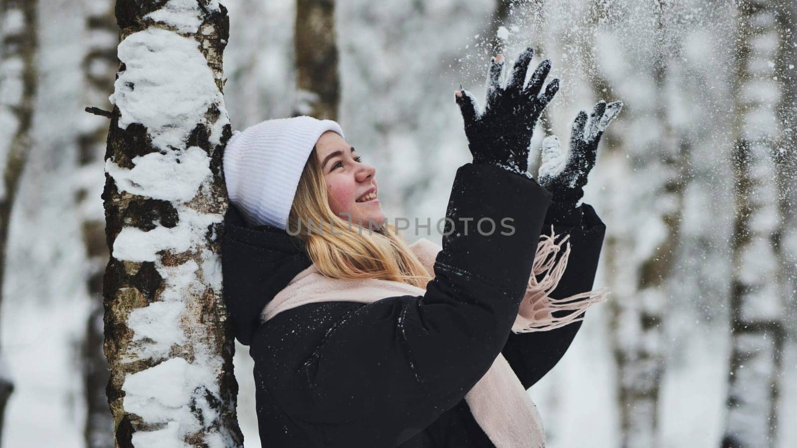 A girl is walking through the woods and kicking up snow in a birch forest