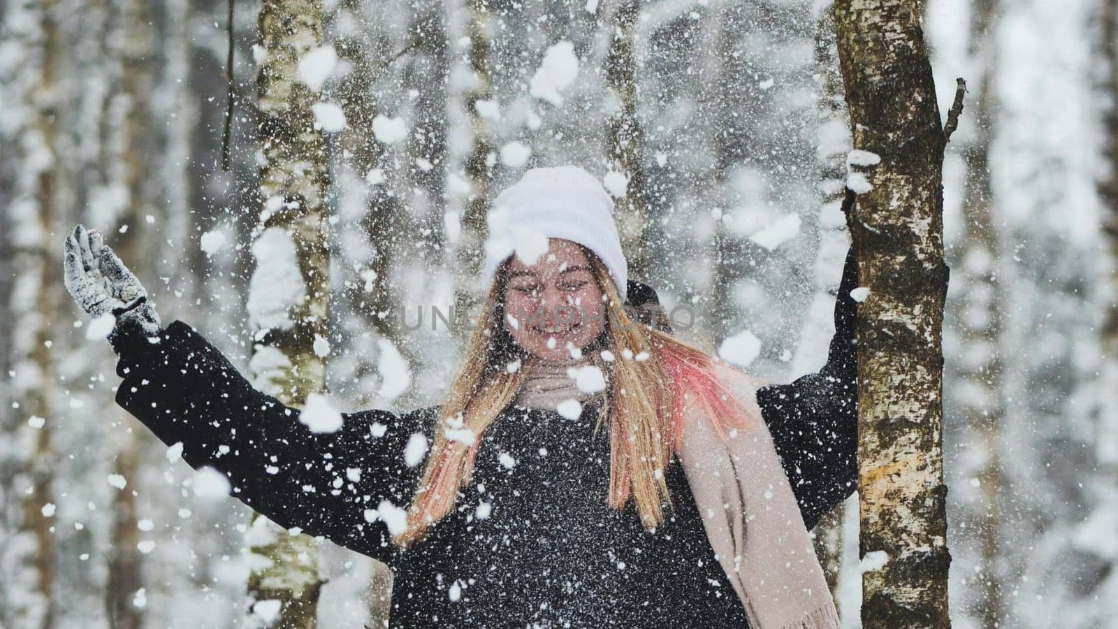 A girl is walking through the woods and kicking up snow in a birch forest