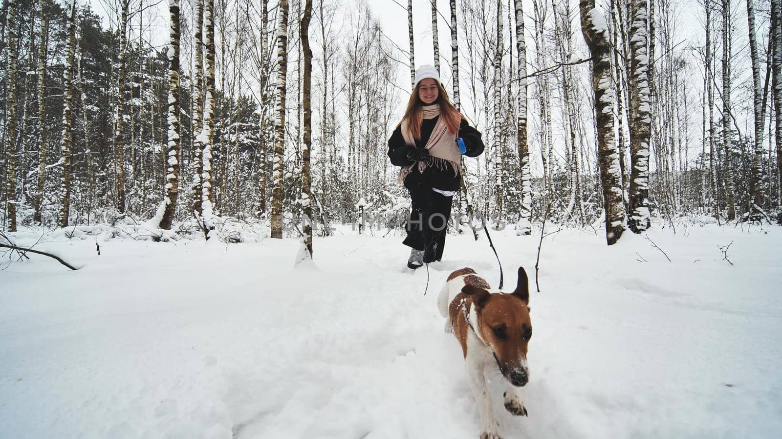 A girl and her Jack Russell Terrier dog are running through the woods