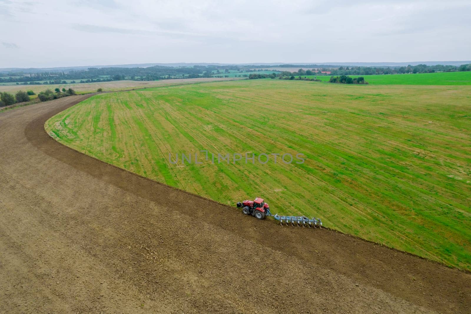 A red tractor plows the land sown with green manure on a near field the railway. Agricultural industry. View from above.