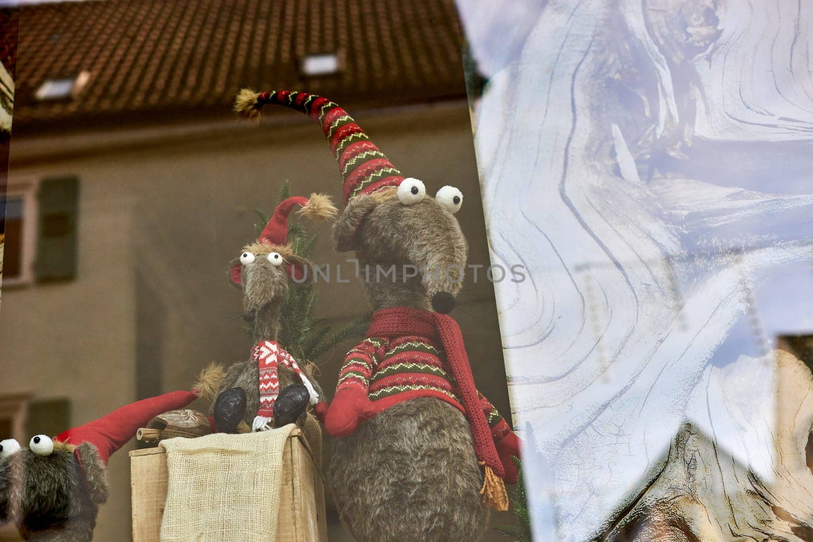 Whimsical New Year's Mouse in Cap and Scarf Stands Behind Store Display. a toy mouse or rat wearing a comical New Year's cap and scarf, playfully standing behind a shop window display. by Andrii_Ko