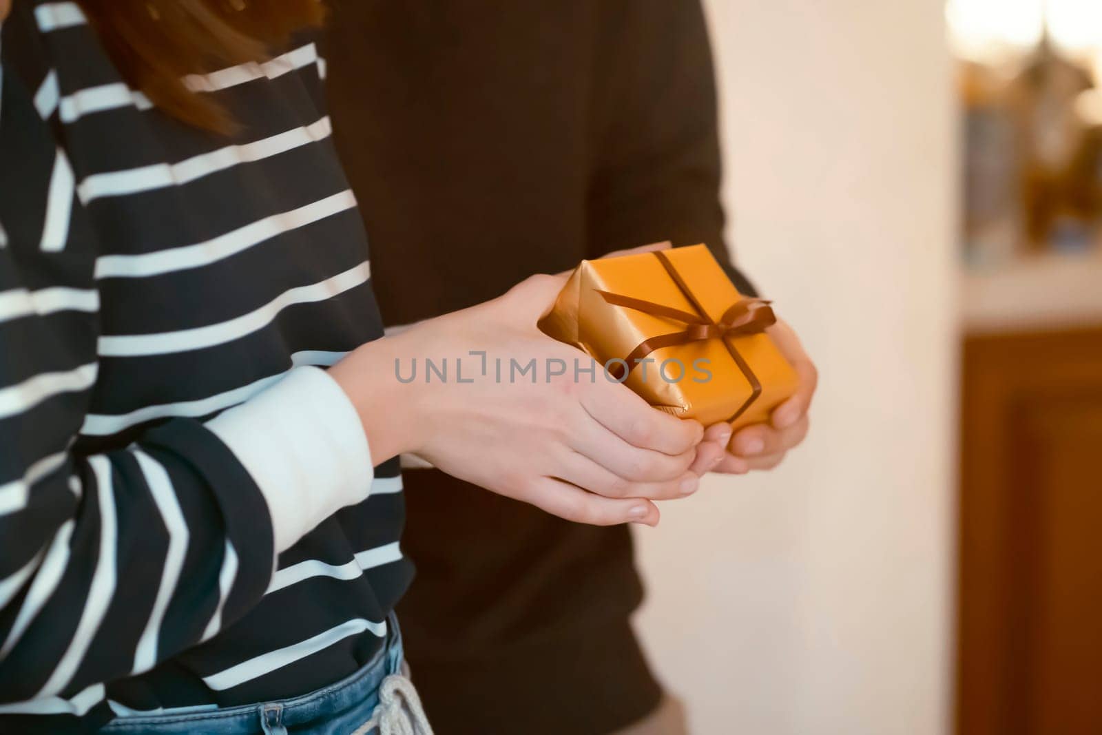 A girl holds a gift in her hands, closeup view. Young man and woman have a good time together, feel unity, a couple celebrating holidays, valentine's day, anniversary, new year or birthday.