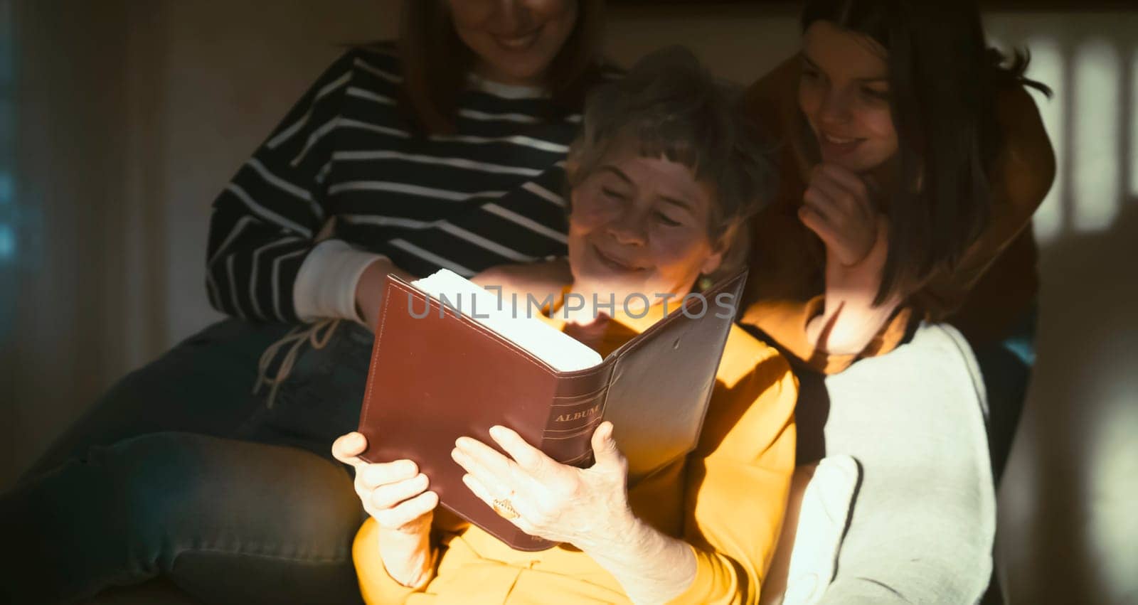 An elderly woman with her granddaughters look the photo album. by africapink
