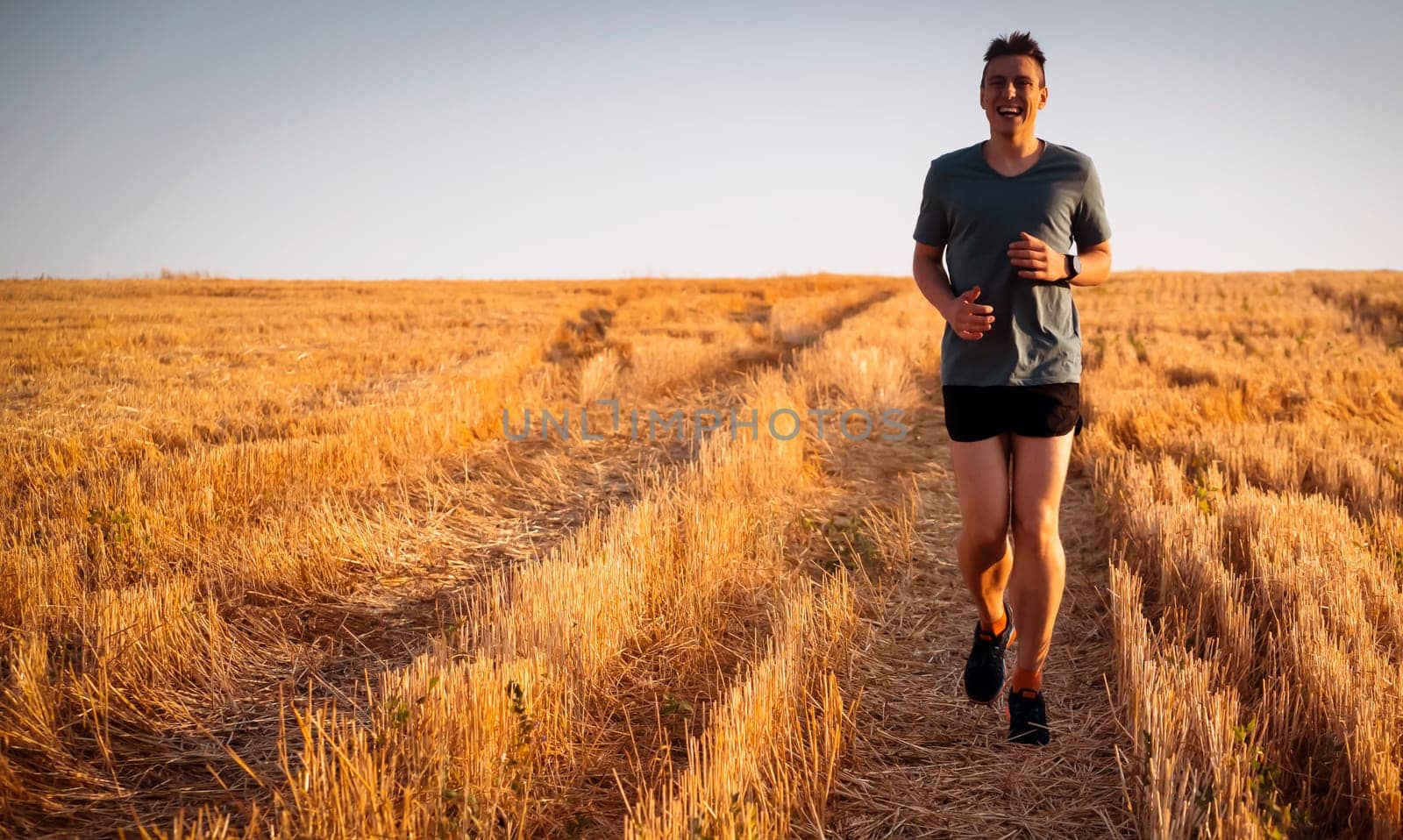 Athlete runner man is running on a trail across a field in a shoe in the sunlight. Fitness and warm-up, young man with sun effect in the background and open space around him.