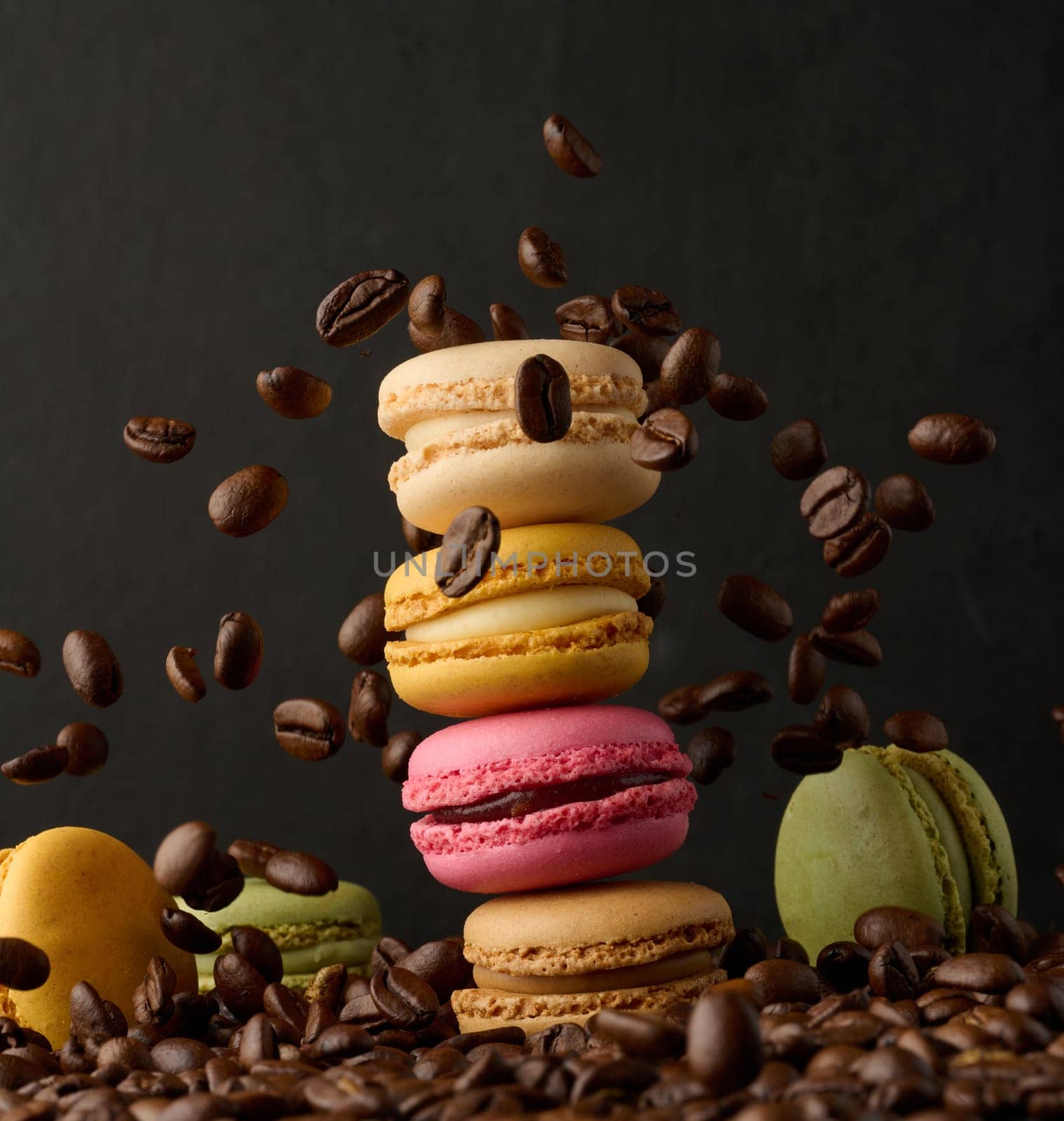 Stack of colorful macarons and flying coffee beans on a black background