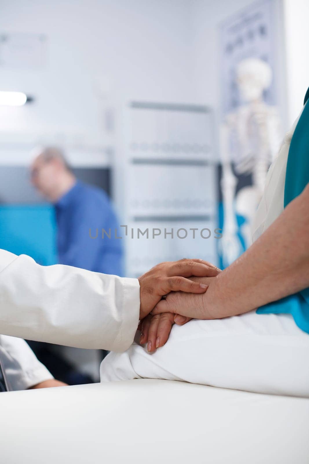 Close-up of doctor with white lab coat grasping the hands of elderly patient at the clinic office. Retired senior person is being examined and diagnosed by a medical practitioner.