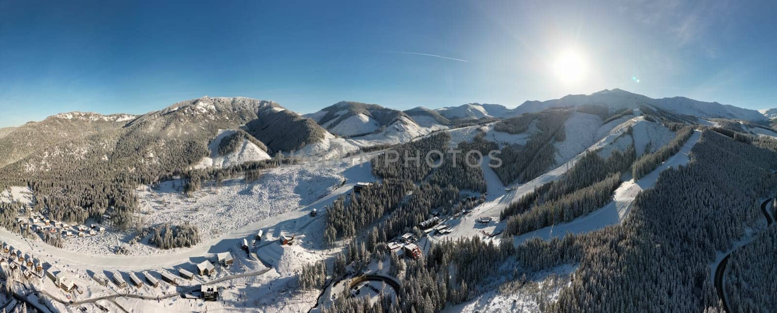 Aerial panoramic winter view of Demanovska Dolina village in Low Tatras mountains, Slovakia. Snowy overhead panorama of countryside rocky landscape with houses, scenic frozen pine forest and road