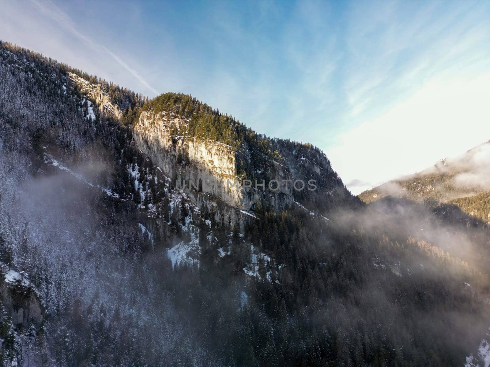 Aerial view of misty pine forest on winter Low Tatras mountain slope in Slovakia. Morning or evening beautiful birds eye scenery with frozen fir trees in snow, panoramic foggy rocky landscape