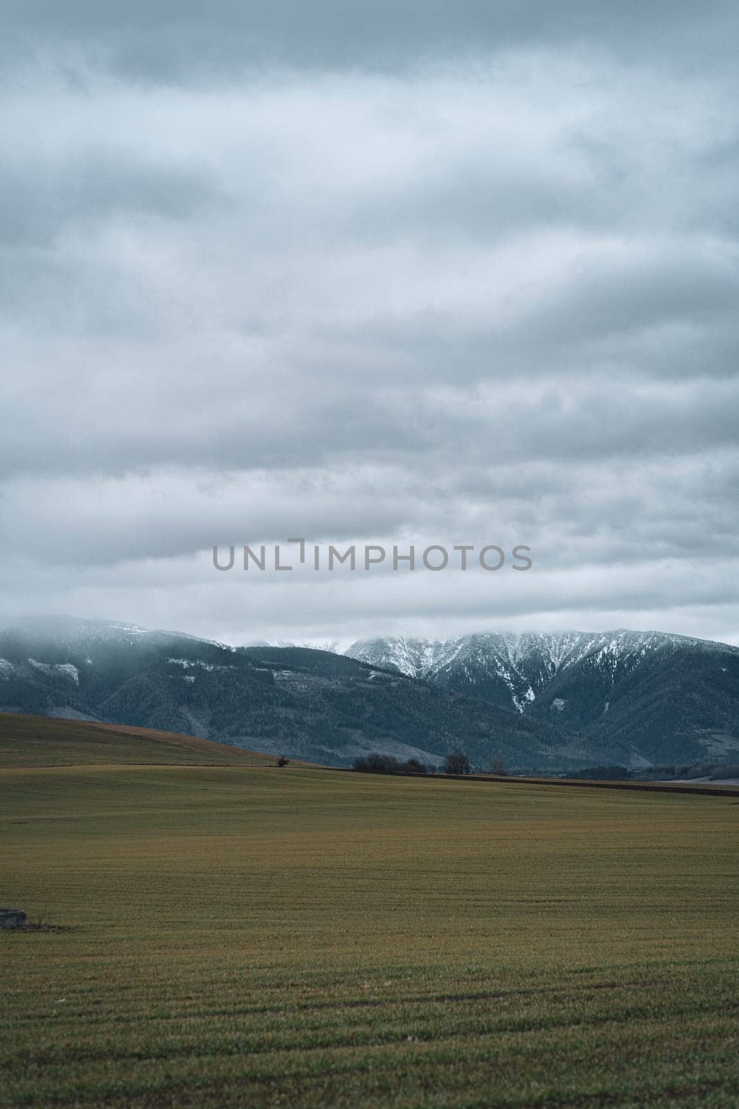 Scenic landscape of Low Tatras mountains, farmland field and cloudy foggy sky in Slovakia