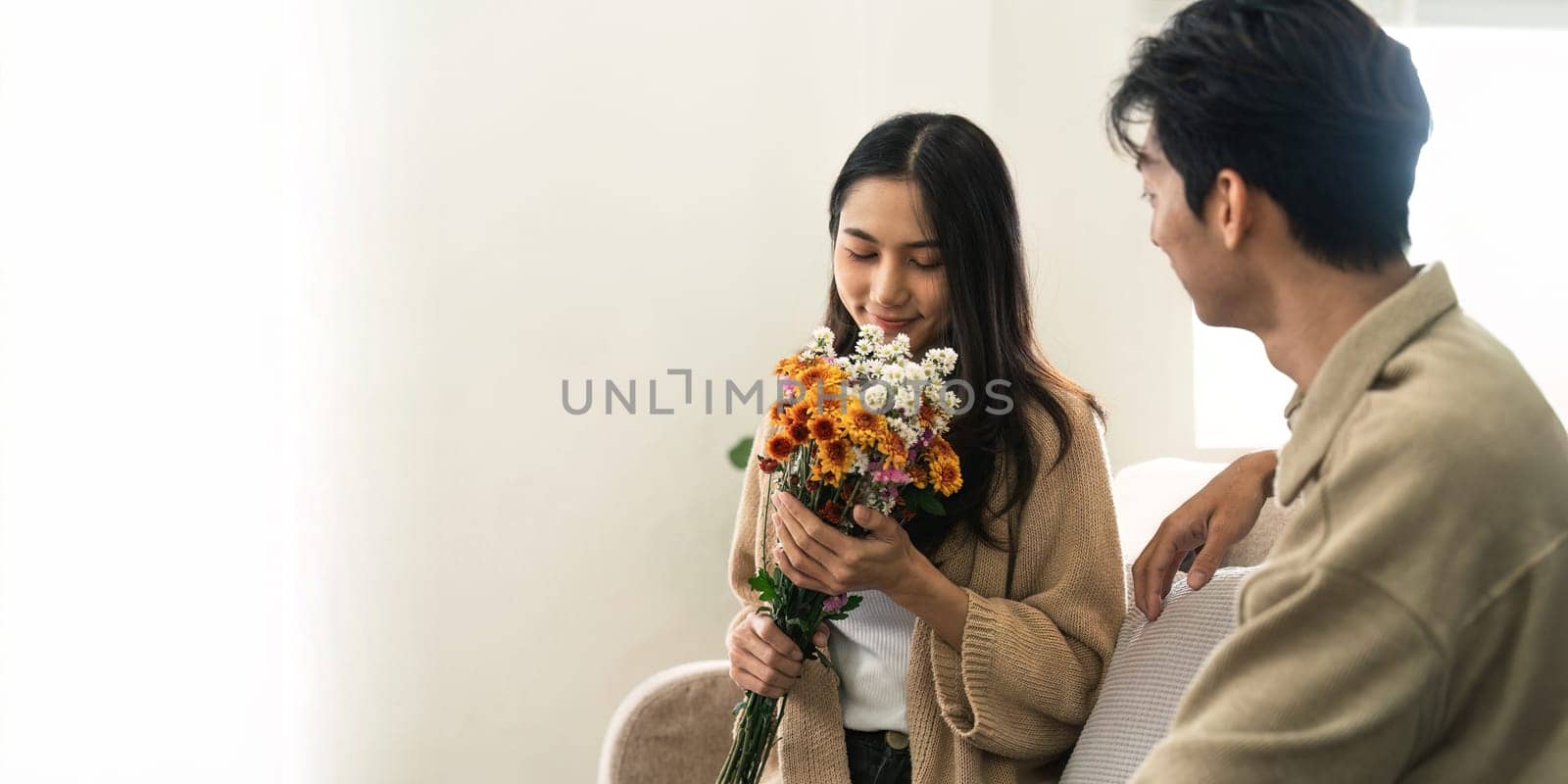 Asian handsome man show the love and give flowers to his girlfriend in living room on valentine day. Lifestyle Concept by nateemee
