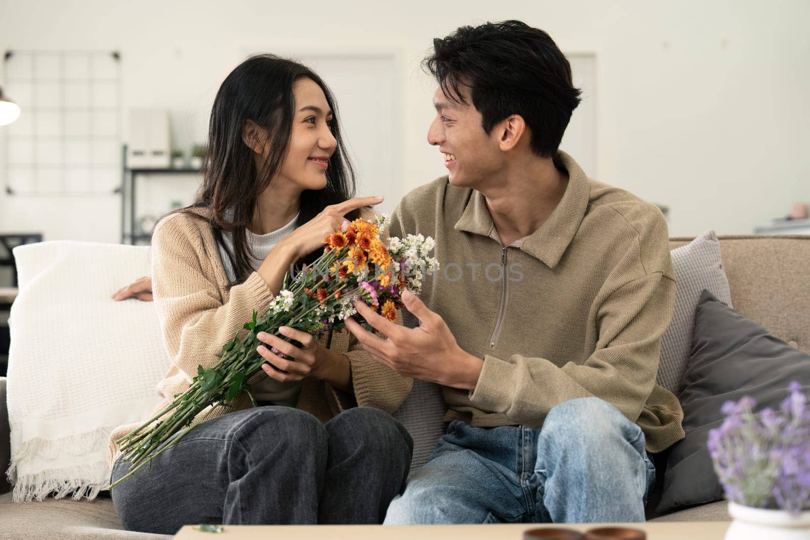 Asian handsome man show the love and give flowers to his girlfriend in living room on valentine day. Lifestyle Concept.