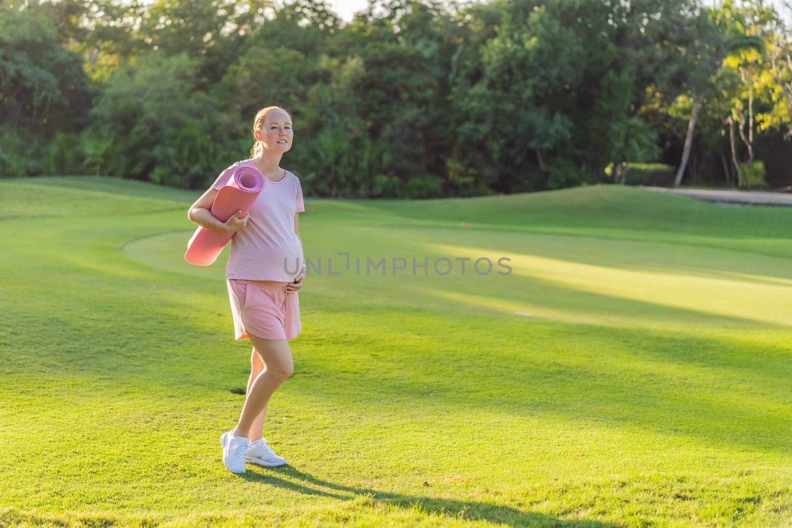 Energetic pregnant woman takes her workout outdoors, using an exercise mat for a refreshing and health-conscious outdoor exercise session.