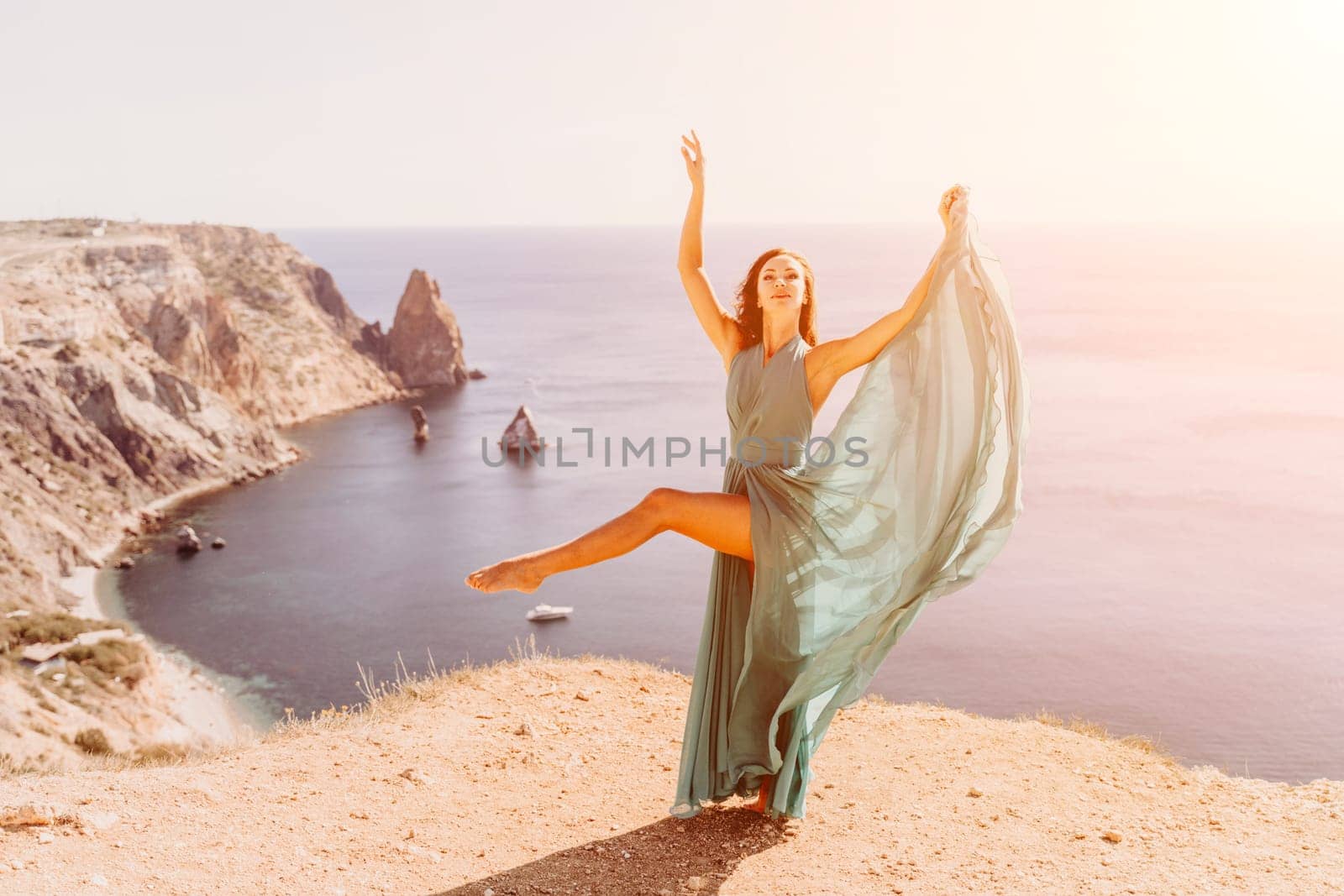 Woman green dress sea. Female dancer posing on a rocky outcrop high above the sea. Girl on the nature on blue sky background. Fashion photo. by Matiunina