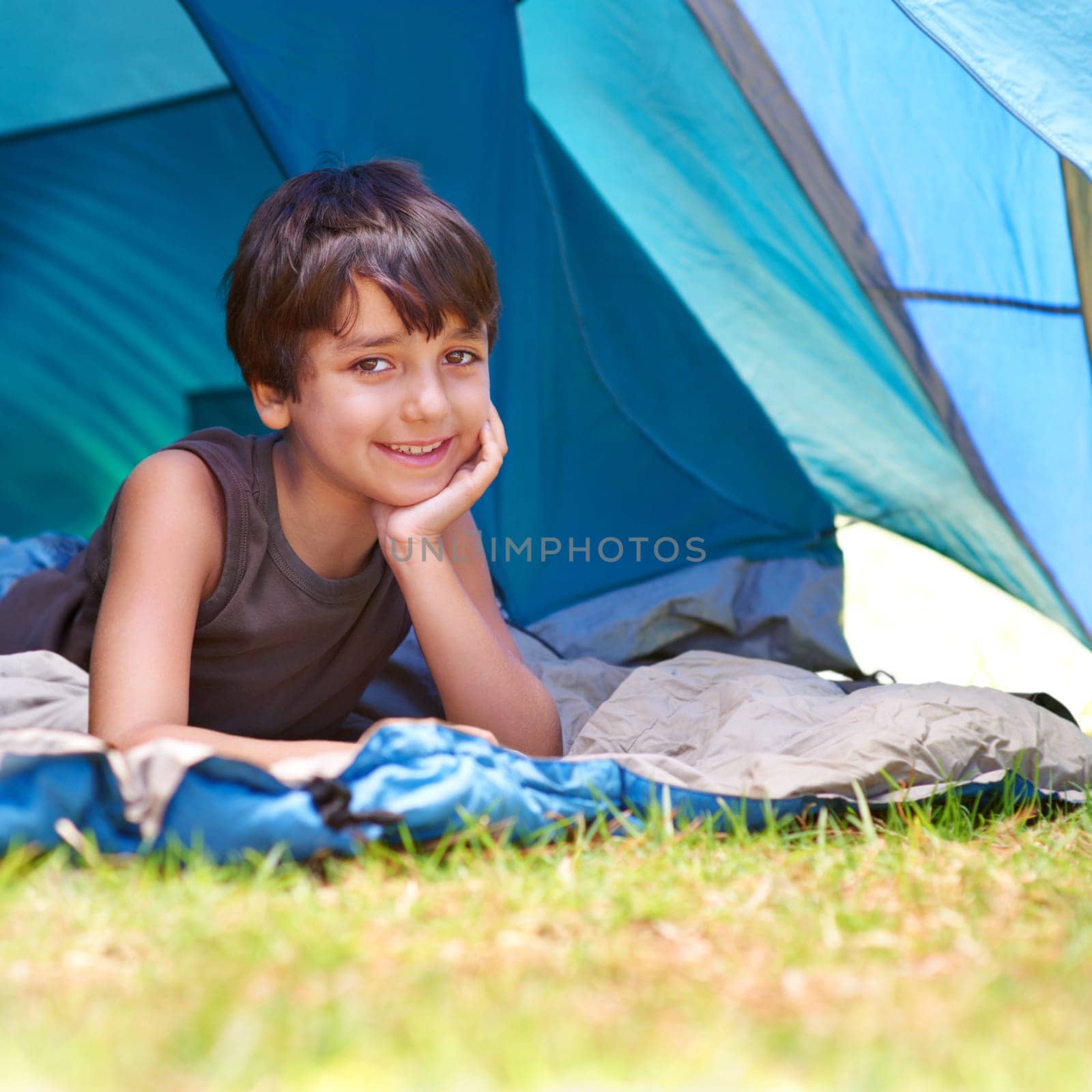 Boy, child and camping, relax in tent and summer vacation with travel and happy in portrait outdoor. Rest on sleeping bag, young camper with smile and adventure in nature, childhood and recreation.