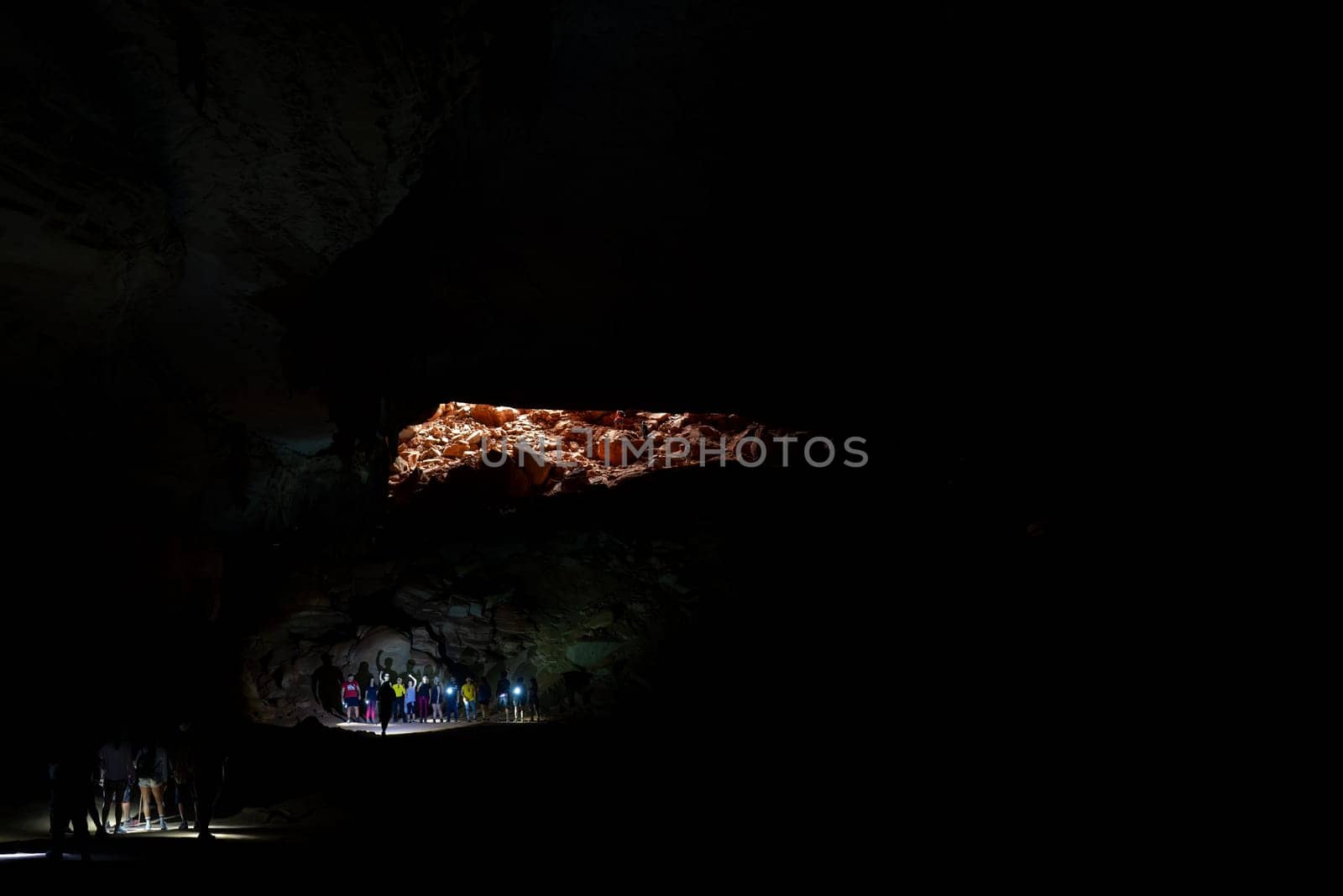 A crowd in a large dark cave lit by a single light.