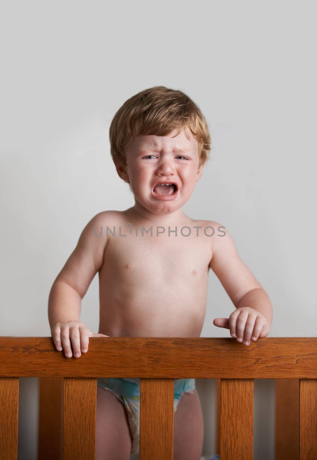Sad toddler, crying and portrait of baby in his crib or home with emotional anger or loss in childhood. Problem, trouble and house with a frustrated young male kid, infant or boy with tears or noise by YuriArcurs
